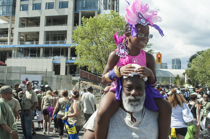 Proud grandfather Arthur Augustine crowns his neck with one of his most precious gifts, his first granddaughter six-year-old Janella. She was giddy with excitement for her very first Caribana three years ago and hasn’t failed to return for each parade that followed. With a grandfather that’s been coming to join in the festivities for the last 40 years, Janella hopes she will one day reach that number, continuing to revisit for a very long time.